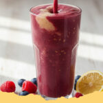 energie booster beeren ingwer smoothie mit haferflocken - Ein Glas Energie Booster Beeren-Ingwer-Smoothie mit Haferflocken, garniert mit frischen Beeren und Minze, auf einem Holztisch.