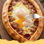 hausgemachte tuerkische pide mit sucuk und ei - Frisch gebackene hausgemachte türkische Pide mit würzigem Sucuk, einem Spiegelei und frischer Petersilie auf einem Holzbrett, bereit zum Servieren.