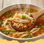 huehnersuppe mit nudeln und gemuese - Eine dampfende Schüssel hausgemachte Hühnersuppe mit goldgelben Nudeln, bunten Gemüsestücken und zartem Hähnchenfleisch, garniert mit frischer Petersilie auf einem Holztisch.