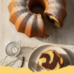 klassischer marmor ruehrkuchen saftig - Ein wunderschön marmorierter, saftiger Gugelhupf, angeschnitten auf einem Kuchengitter, verziert mit Puderzucker. Im Hintergrund eine Tasse Kaffee und eine Blumenvase.