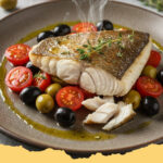 mediterrane seebarschfilets mit tomaten oliven gemuese - Zwei gebackene Seebarschfilets auf einem Bett aus Tomaten, Oliven und Zucchini, garniert mit frischen Kräutern in einer Auflaufform.