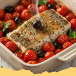 mediterraner gebackener seelachs mit kirschtomaten - Ein Blech mit goldbraun gebackenem Seelachs umgeben von geplatzten roten Kirschtomaten, frischen Kräutern und Zitronenspalten, appetitlich angerichtet