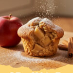 fluffige apfel zimt muffins - Ein Stapel von frisch gebackenen, fluffigen Apfel-Zimt Muffins auf einem Holztisch mit einer Zimtstange und Apfelspalten im Hintergrund.