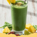 power gruener smoothie mit spinat ingwer und ananas - Ein großes Glas mit leuchtend grünem Power Grüner Smoothie, garniert mit Ananasstückchen und einem Spinatblatt.