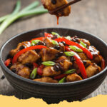 schnelles asiatisches haehnchen pfannengericht mit schwarzer bohnensauce - Ein Teller mit schnellem asiatischem Hähnchen Pfannengericht mit schwarzer Bohnensauce, garniert mit Sesam und Frühlingszwiebeln, serviert mit Reis.