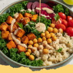 vegane buddha bowl mit ofensuesskartoffel und tahin dressing - Eine farbenfrohe vegane Buddha Bowl mit Ofensüßkartoffeln, Kichererbsen, frischem Gemüse und Tahin-Dressing auf einem Holztisch.