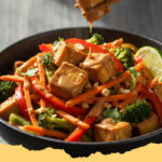 vegane gemuesepfanne mit tofu und erdnuss sauce - Eine köstliche vegane Gemüspfanne mit Tofu und cremiger Erdnusssauce in einer Schüssel, garniert mit Koriander und Erdnüssen.