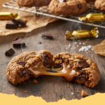 weiche schoko hafer cookies mit salzkaramell tropfen - Ein Stapel weicher Schoko Hafer Cookies mit geschmolzenen Salzkaramell Tropfen auf einem Holzbrett mit einer Tasse Kaffee im Hintergrund.